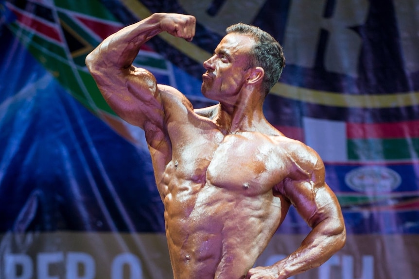 A shirtless bodybuilder posing and flexing his bicep