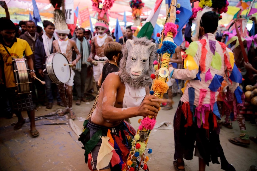 A farmer wears an animal mask and dances in protest.