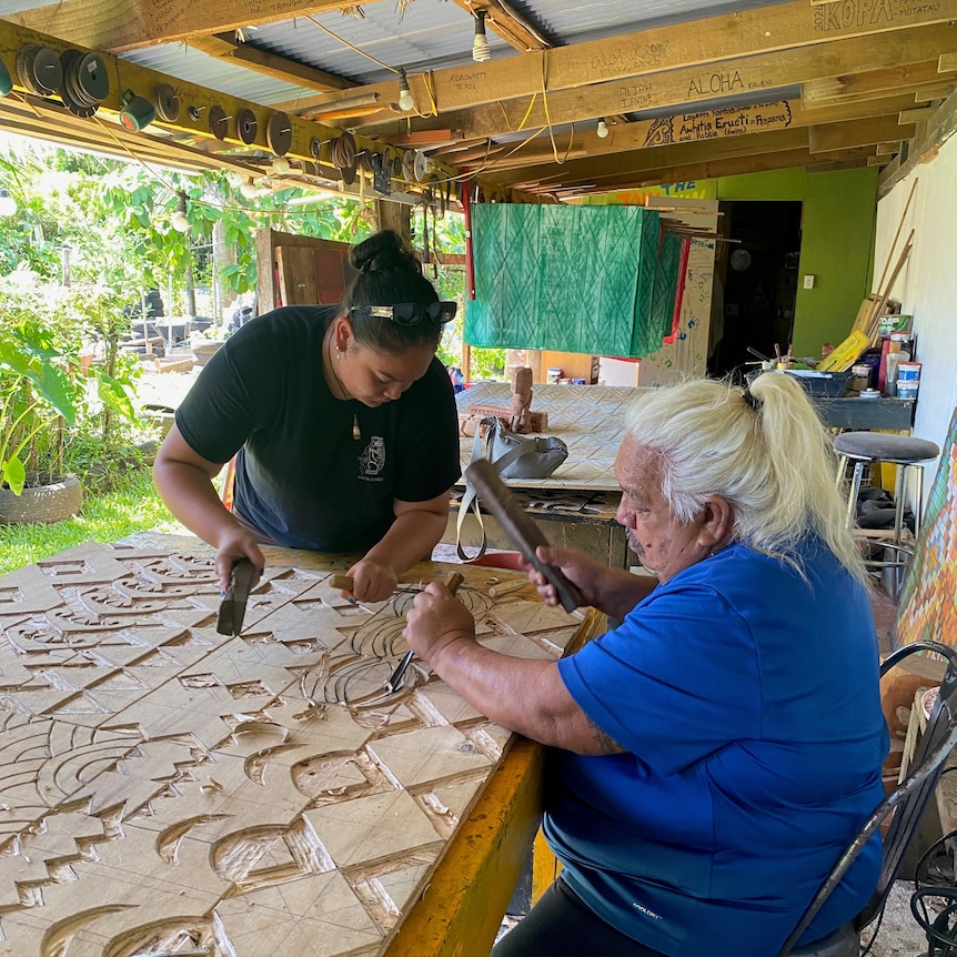 A woman and a man use tools to carve patterns into a wooden board
