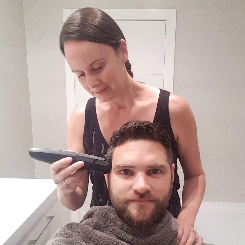 A man purses his lips while a woman uses a shaver on the side of his head
