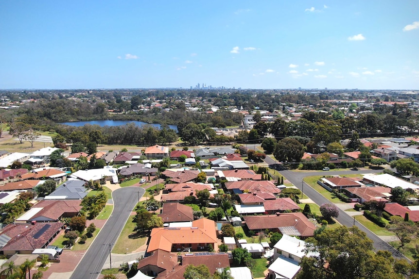 An aerial shot of a city skyline in the distance, with houses and parklands in the foreground