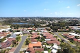An aerial shot of a city skyline in the distance, with houses and parklands in the foreground