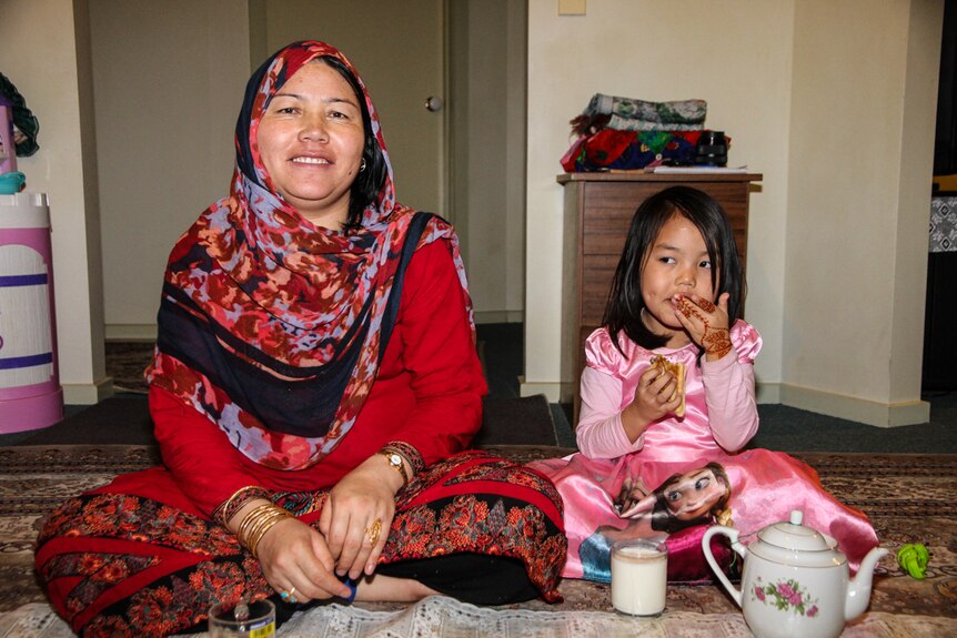 Woman and girl sitting on a mat on the floor enjoying a cup of tea and a glass of milk at home.
