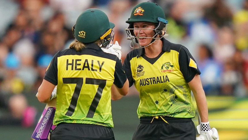 Beth Mooney smiles as she high-fives Alyssa Healy, whose back is to the camera.