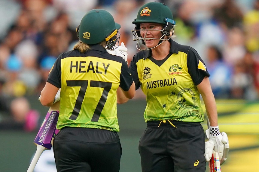 Beth Mooney smiles as she high-fives Alyssa Healy, whose back is to the camera.