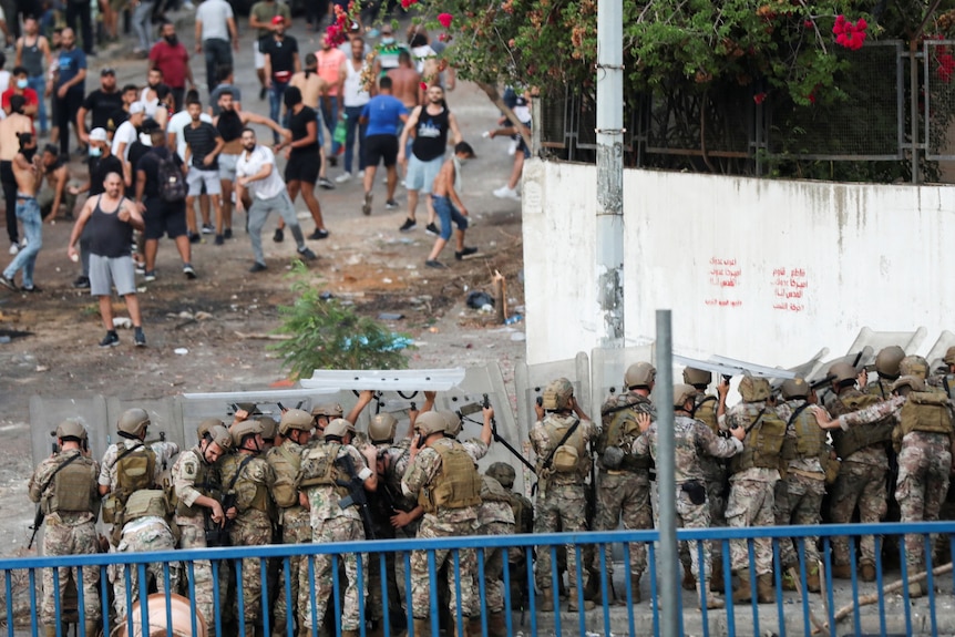 Soldiers take cover behind shiels as protestors throw stones.