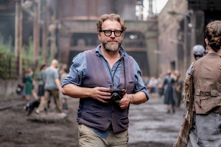 Uli, who wears glasses and holds a camera, on a Hunger Games set.