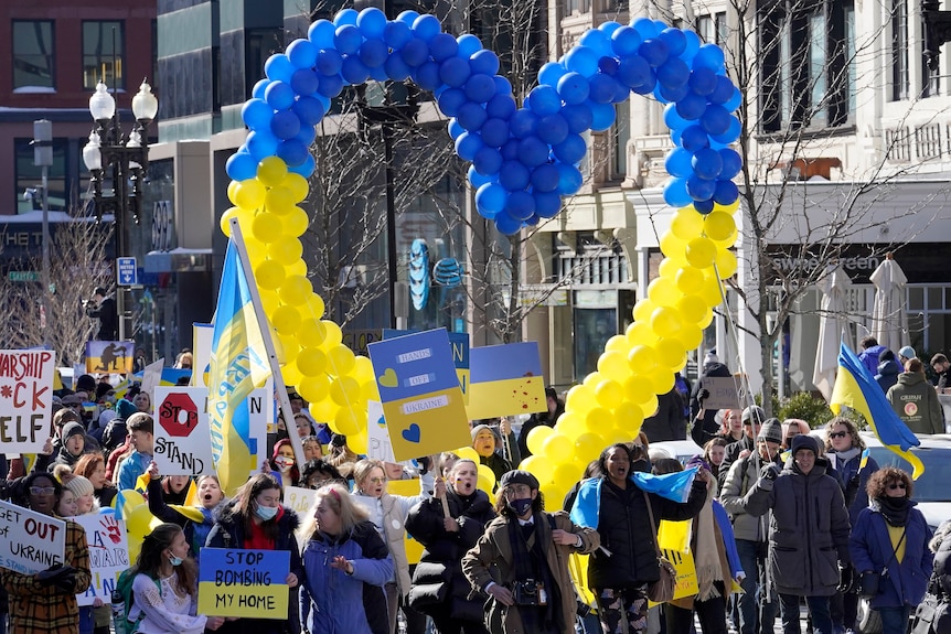 Protesters walk with signs and a large heart made out of balloons in the colours of the Ukrainian flag.
