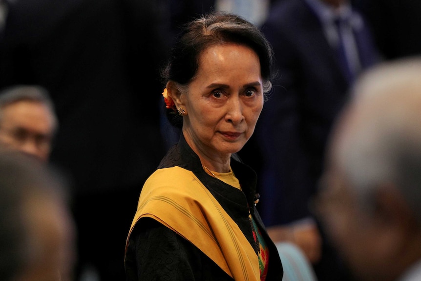 Myanmar State Counsellor Aung San Suu Kyi looks at the camera wearing a gold yellow scarf draped.