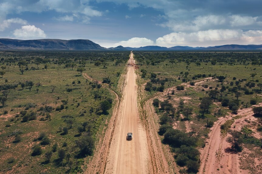 A long outback road with a lonely car on its path