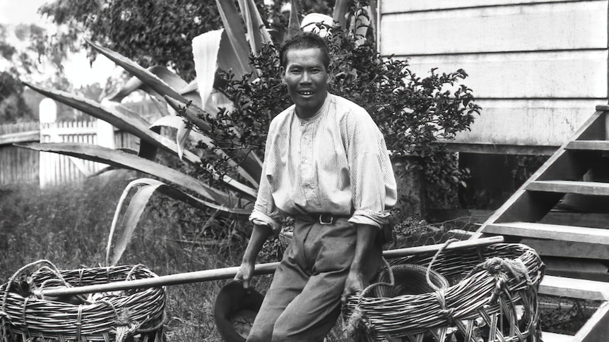 A man leans on a large basket outside of a house.