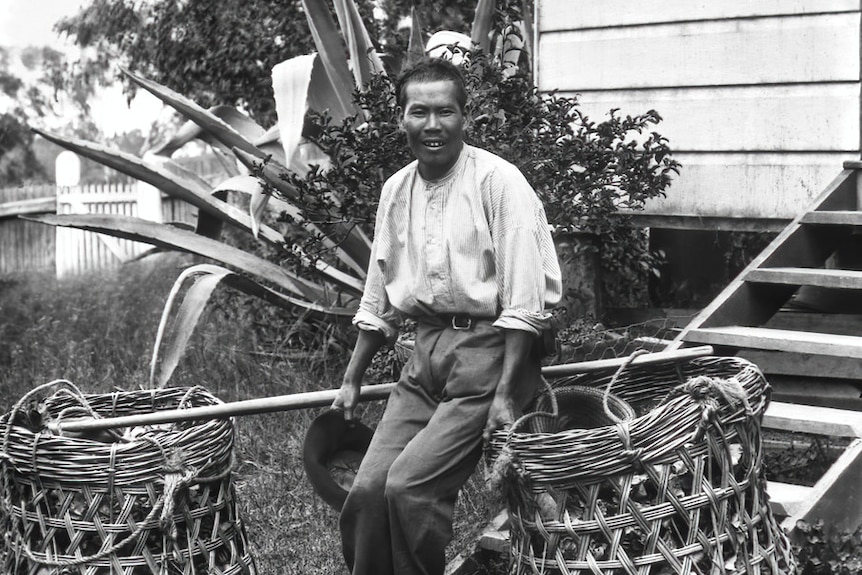 A man leans on a large basket outside of house.