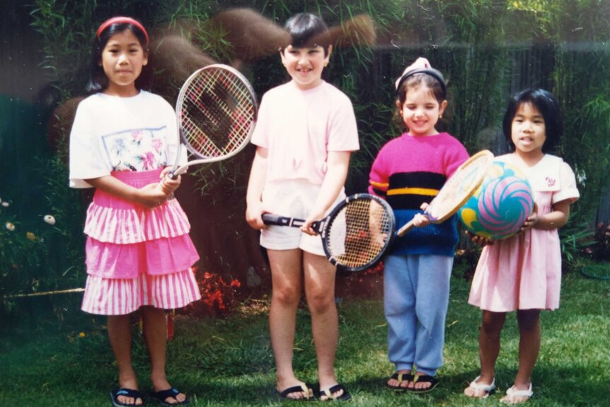 Tuanh Nguyen, left, wears a pink tennis skirt and holds a tennis racquet next to three other children in a backyard garden.