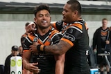 An NRL player stands next to the corner post after scoring a try, receiving a hug from a teammate.