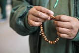 A close up shot of a prisoner's hands holding prayer beads, known as Misbaha, used to count prayers.