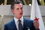 California Governor Gavin Newsom, wearing a jacket and tie and standing behind a podium, answers questions at a news conference