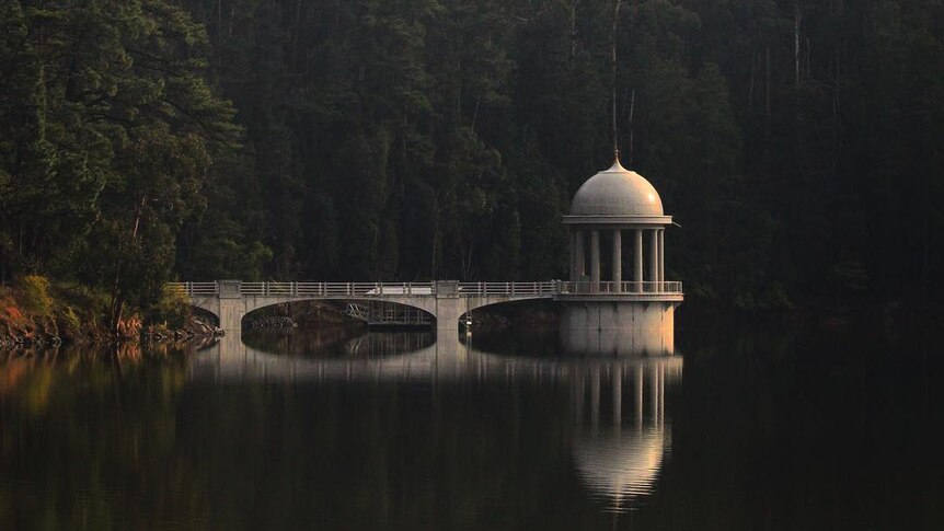 A pier and rotunda extend out in to a dam and create a reflection.