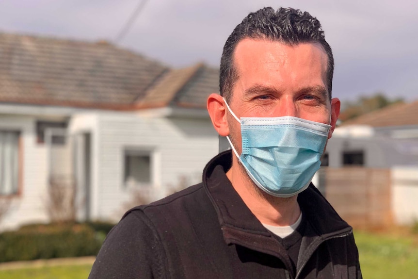 A man in his thirties wears a mask outside his home in colac