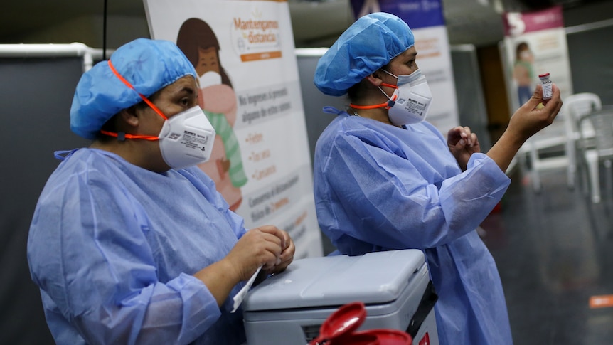 Nurses in PPE prepare doses of the vaccine.