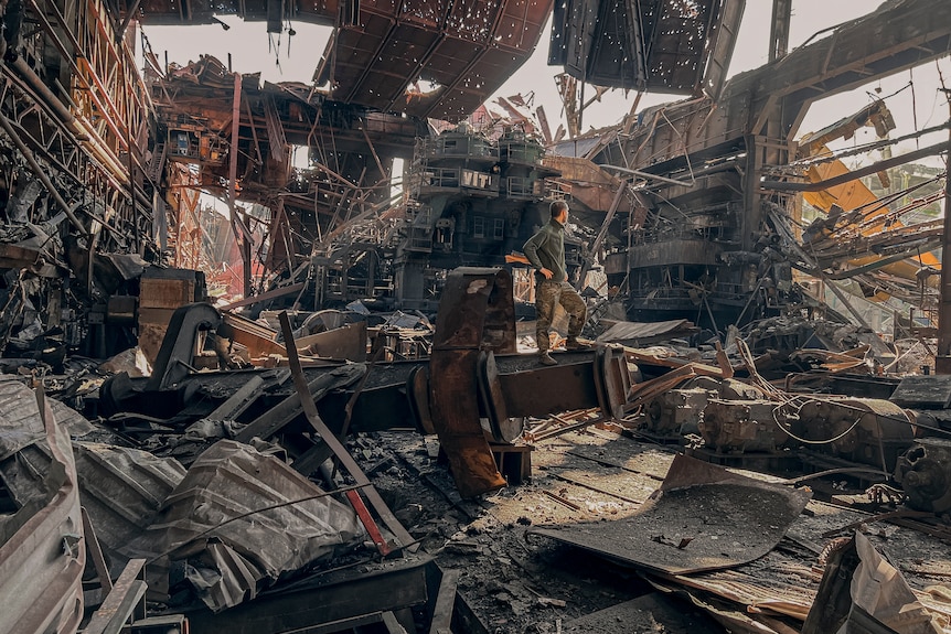 一个男人站在钢铁厂弯曲的废墟中。
