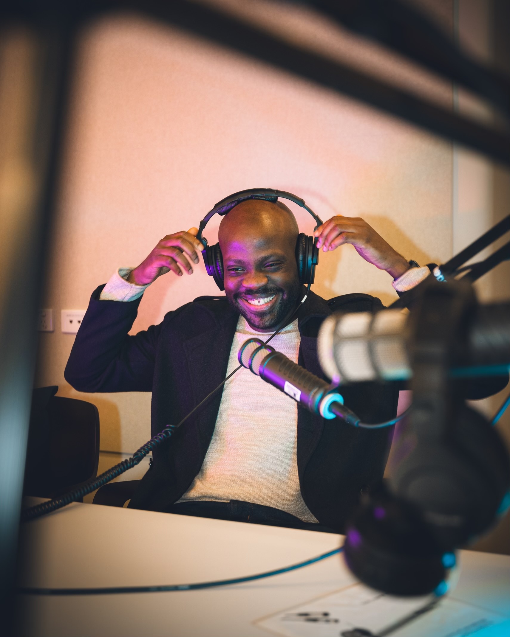 Ri'chard putting headphones on in a podcast studio, smiling, microphone in front of him