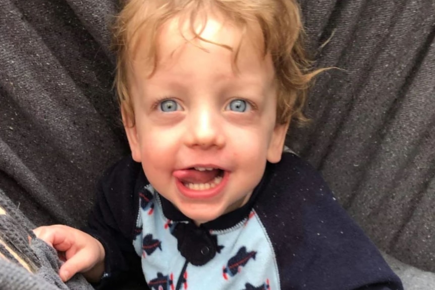 A photo of a toddler with blonde hair and blue eyes looking into the camera.