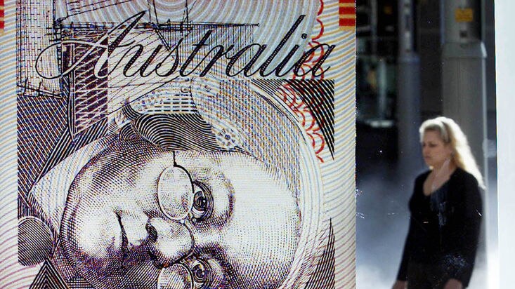 A woman walks near a large mock Australian currency note displayed in a Reserve Bank of Australia window.