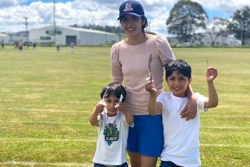 A Nepalese woman in a cap with two young children at a cricket ground