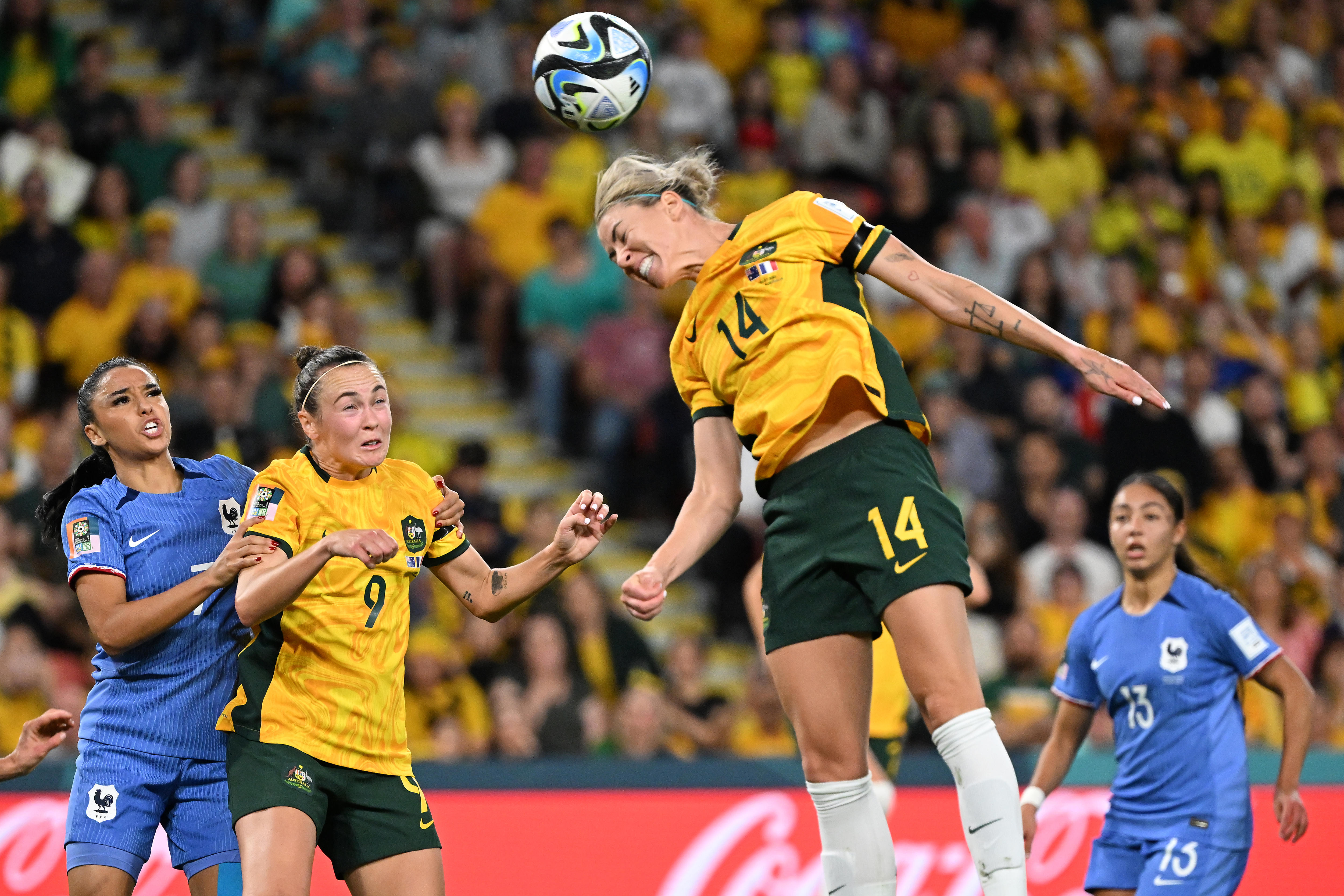 Player no 14 jumps up to head a soccer ball with a grimace on her face