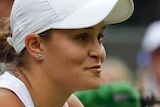 Ash Barty leans on the net holding her racquet with a smile on her face