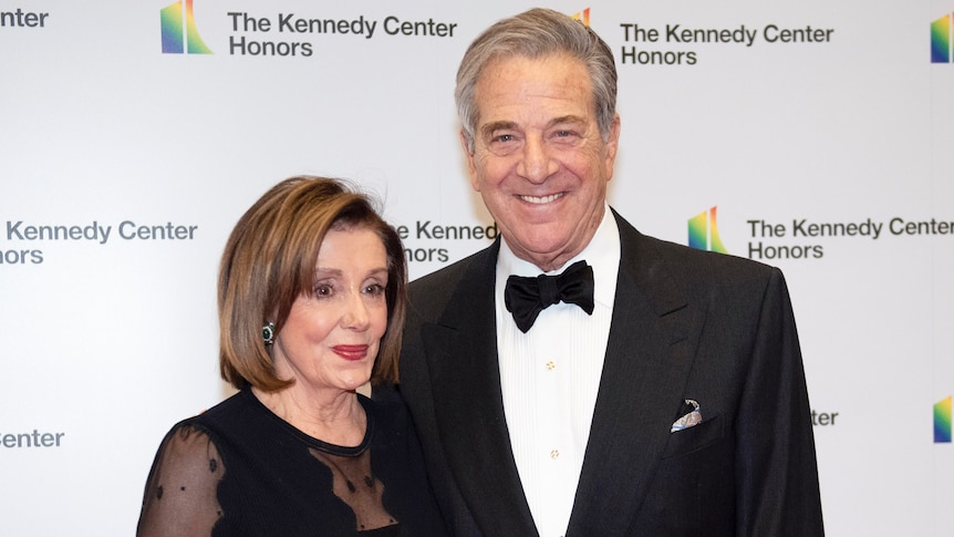 An elderly couple in formal black attire smile as they pose for a photo.