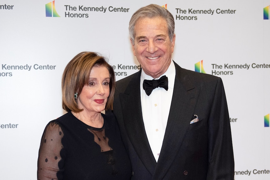 An elderly couple in formal black attire smile as they pose for a photo.