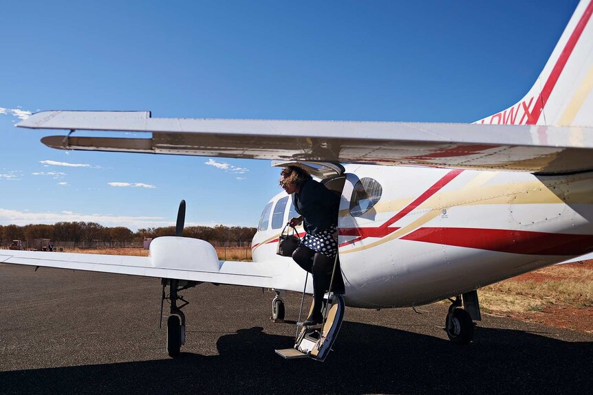 Leanne Liddle walks off the steps of a small plane to step onto the tarmac in Yuendumu on a sunny day.