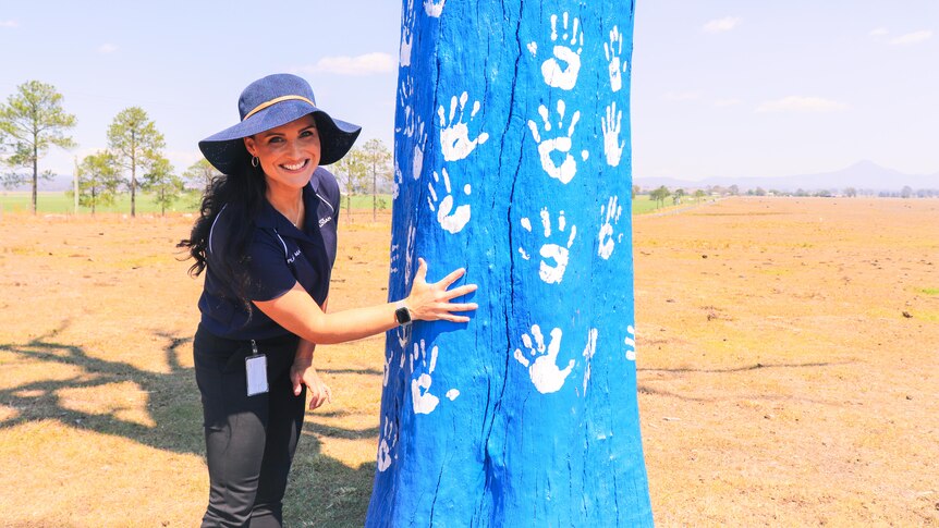 A woman places a hand print on a tree painted blue.