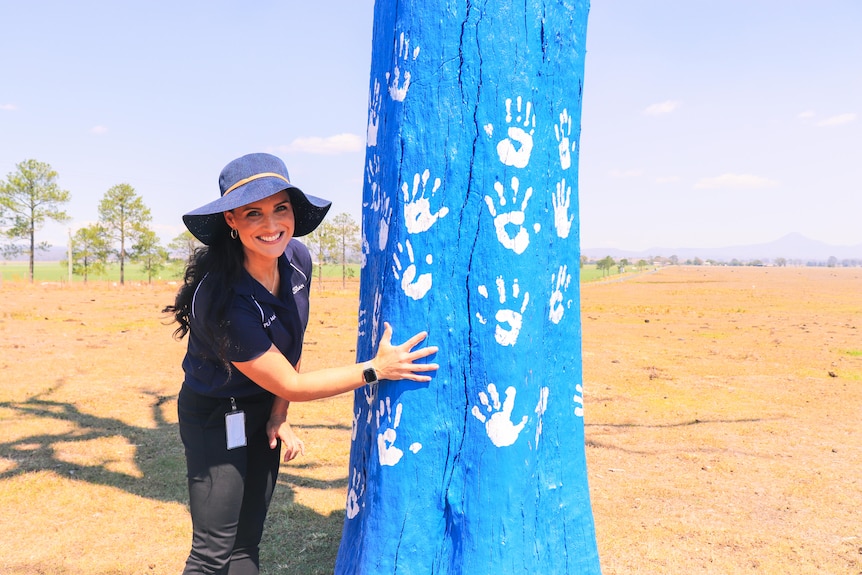 a woman places a hand print on a tree painted blue