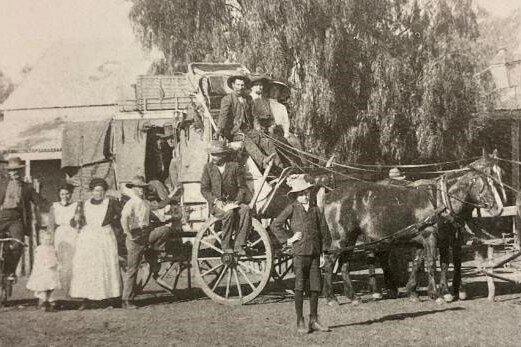 An old black and white photo of people standing around a horse drawn coach outside a hotel.