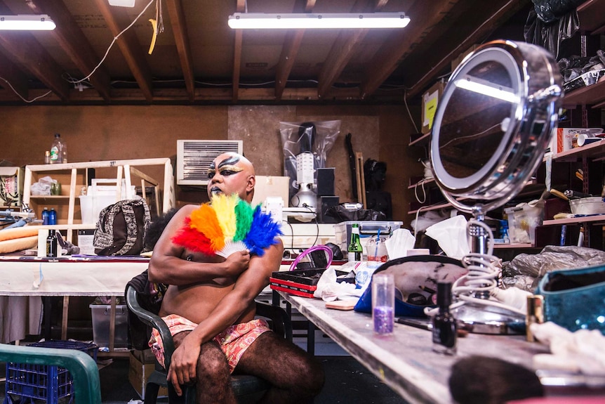 Colour photograph of Dallas Webster with rainbow fan, getting ready for a drag performance.