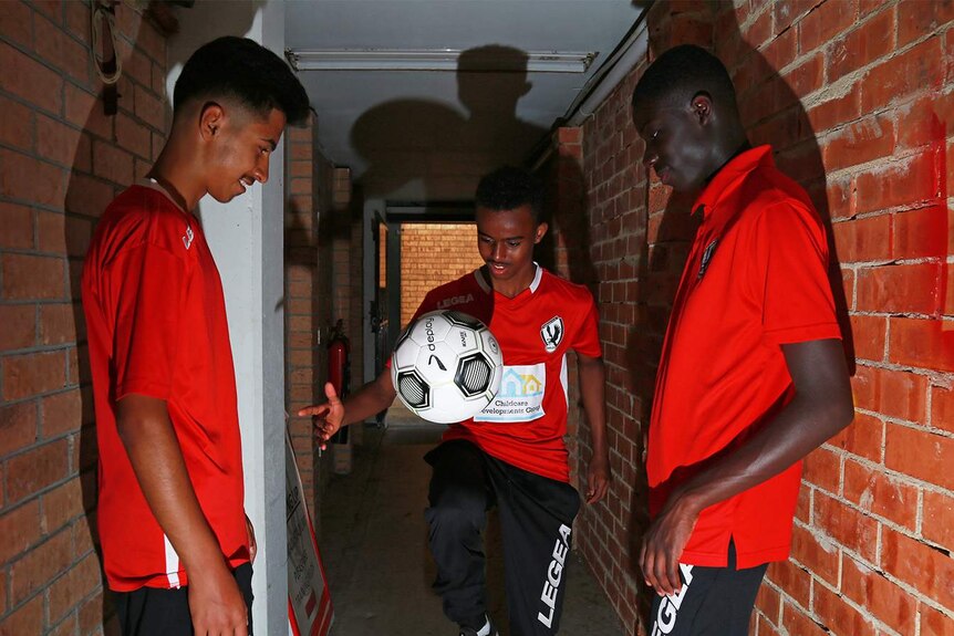 Three boys in a tunnel kick a soccer ball between each other.