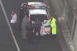 Police officers huddle around the car on the Logan Motorway.