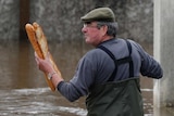 A man holds baguettes while standing in flood water in Paris.