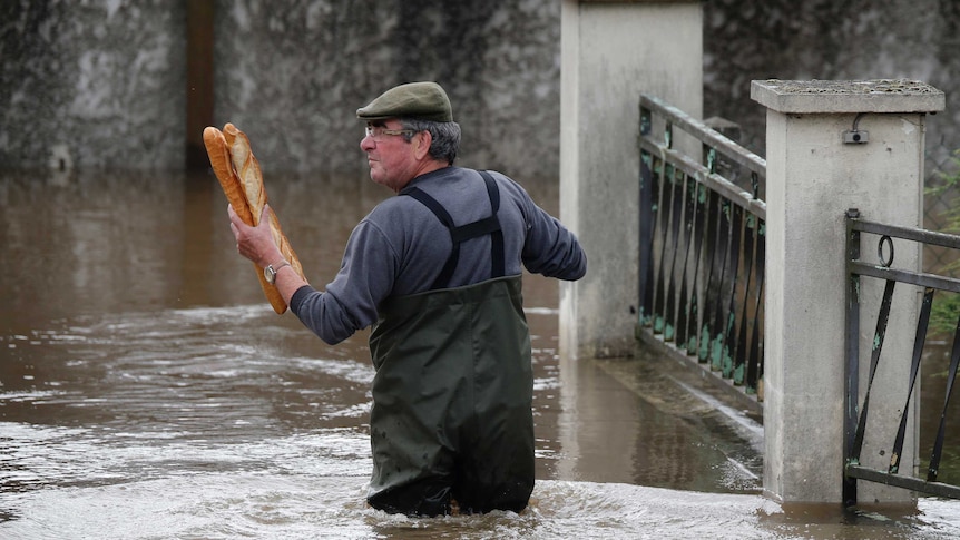 A man holds baguettes while standing in flood water in Paris.