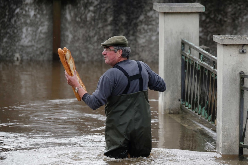 A man holds baguettes while standing in flood water in Paris.