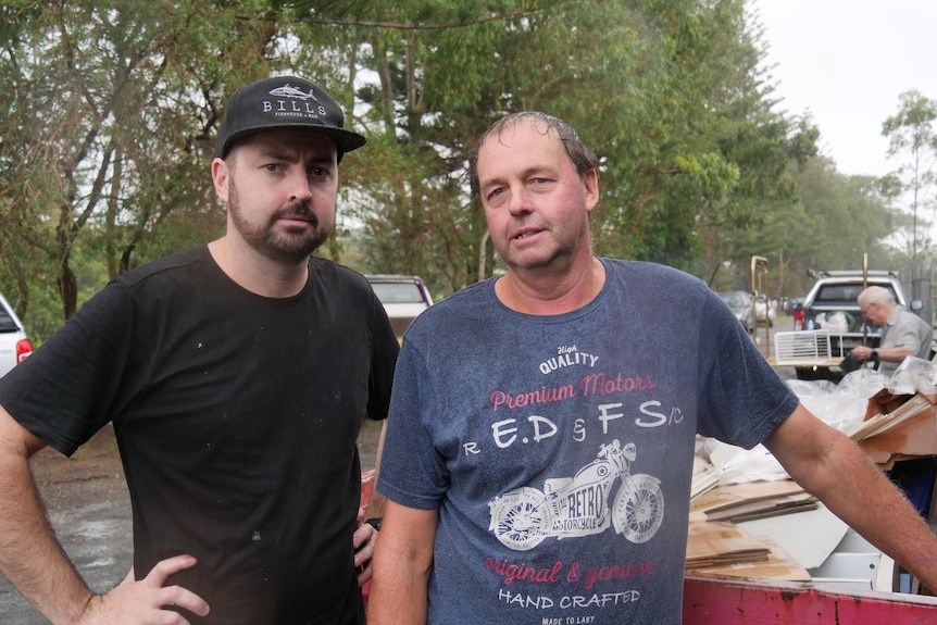 Two men, one young man and his father in the rain with rubbish in the background