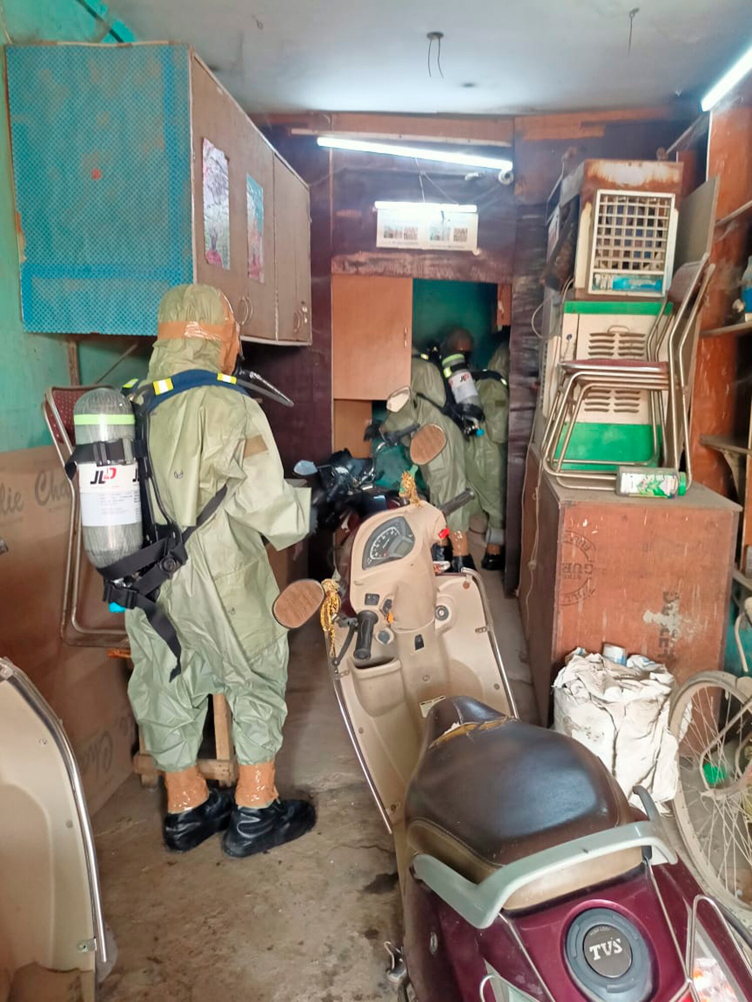 A person in a hazmat suit walks through a small apartment room. 