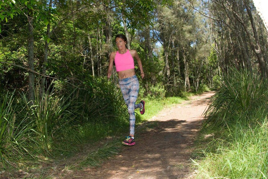 Woman in pink top and colourful leggings runs in forest