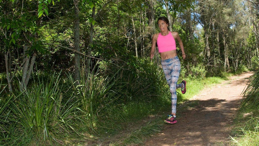 Woman in pink top and colourful leggings runs in forest