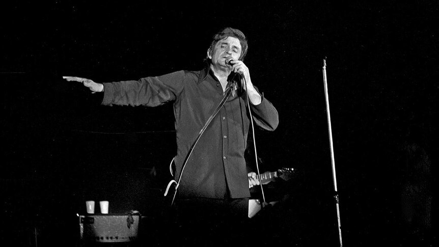 Black and white image of Johnny Cash performing onstage.