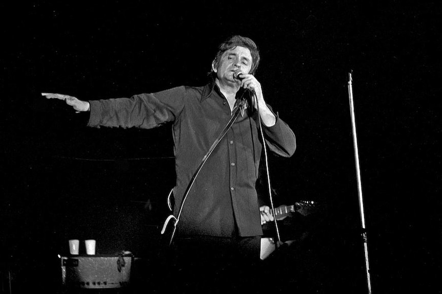 Black and white image of Johnny Cash performing onstage.