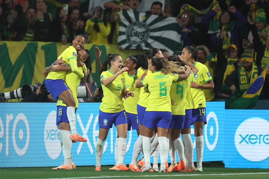 A Brazilian player leaps into a goalscorer's arms as her team celebrates.