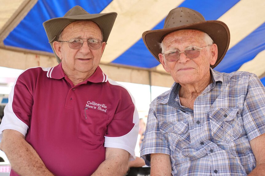 Two older gentlemen sitting under a stiped awning